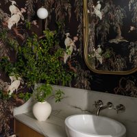 A bathroom vanity features a white oval vessel sink set atop a marble vanity. Dark wallpaper with cranes sitting on tree branches covers the walls.